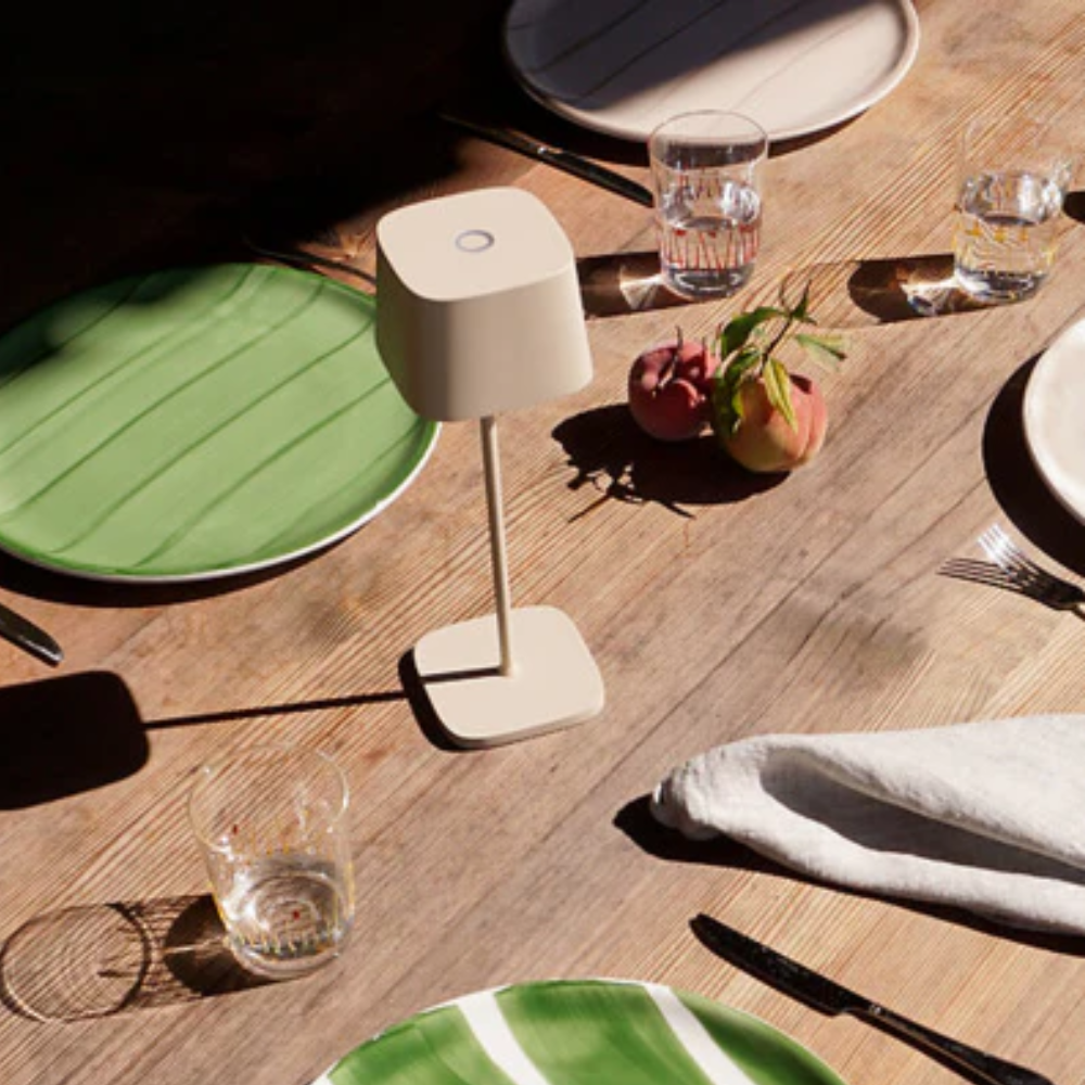 Beige table lamp in matte material, with square base and plate, glasses with water, two red fruits with leaves on wood table