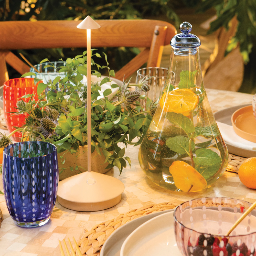 Matte beige table lamp with round base and slim stem, transparent vase with water, green leaves and orange slices, glasses
