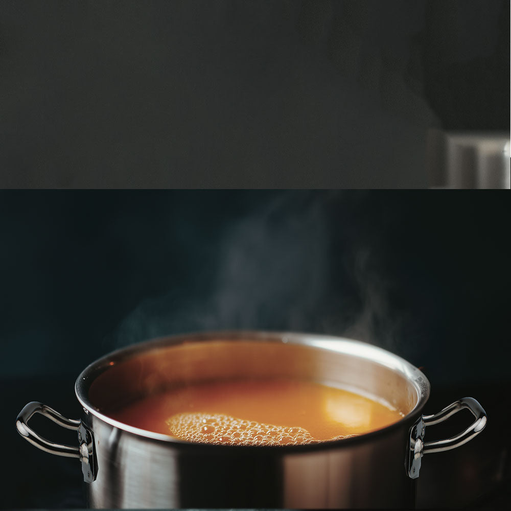 Roestvrijstalen pan met handgrepen, met hete dampende bouillon, op donkere achtergrond.