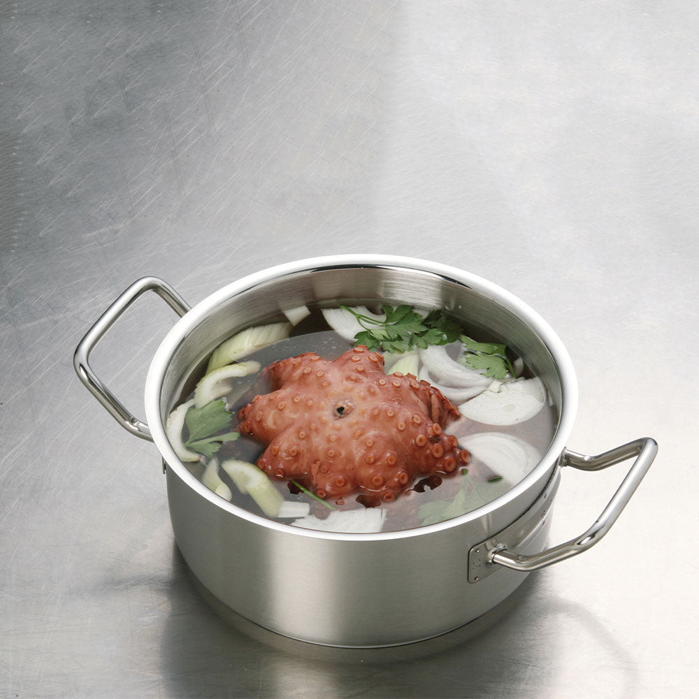 Stalen pan met bouillon, stuk octopus en groenten zoals ui en peterselie op grijs metalen oppervlak.