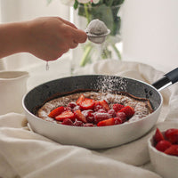 Schokoladenkuchen in weißer Pfanne mit dunklem Rand, garniert mit frischen Erdbeeren und Himbeeren, mit Puderzucker bestäubt.