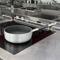 Frying pan with black non-stick interior coating and metal handle with black grip on black induction cooktop in kitchen