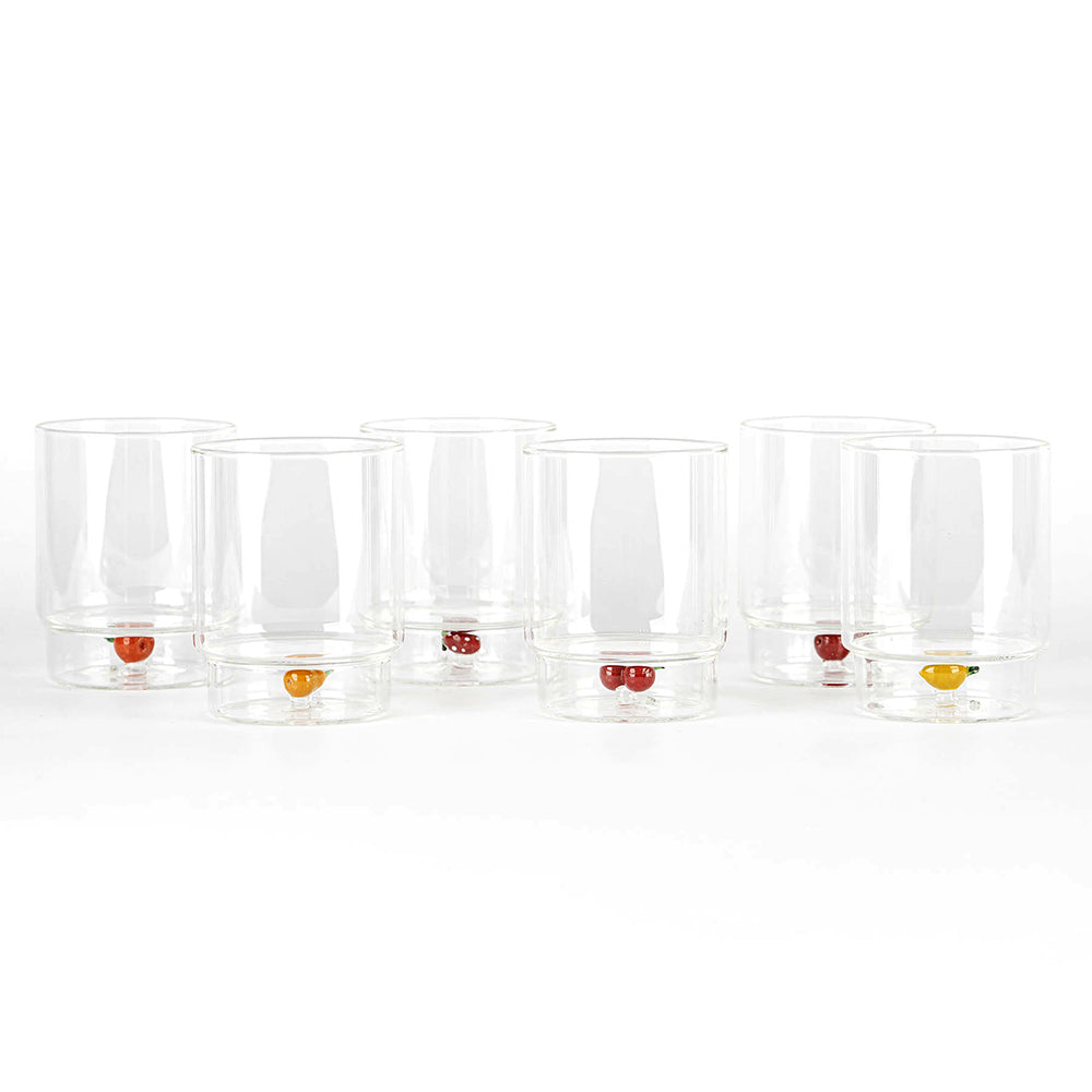 Set di sette bicchieri trasparenti in vetro con piccoli decori a forma di frutta colorata alla base, su sfondo bianco.