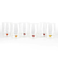 Set di sette bicchieri trasparenti in vetro con piccoli decori a forma di frutta colorata alla base, su sfondo bianco.