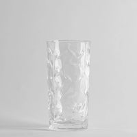 Transparentes Glas mit unregelmäßiger Oberfläche, gewelltem Effekt, auf neutralem grauem Hintergrund.