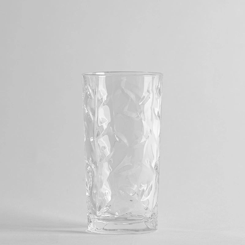 Transparentes Glas mit unregelmäßiger Oberfläche, gewelltem Effekt, auf neutralem grauem Hintergrund.