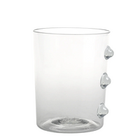 Verre transparent en verre avec trois protubérances rondes sur le côté droit, fond blanc.