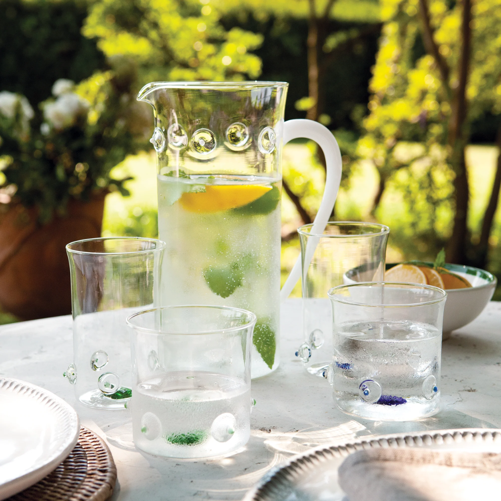 Caraffa e bicchieri di vetro con acqua e fette di limone su tavolo all'aperto in giardino soleggiato