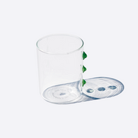 Verre transparent en verre cilindrico avec three small vert petal-shaped embossments, ombra sur the light background.