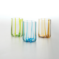 Tre bicchieri di vetro trasparente con strisce verticali colorate in verde, azzurro e arancione su sfondo bianco.