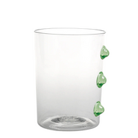 Verre transparent en verre avec trois décors verts en forme de cœur sur un côté, fond blanc.