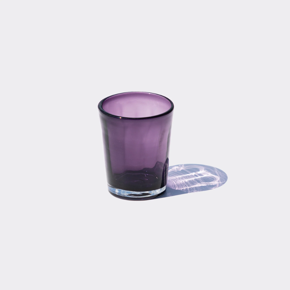Transparent purple glass tumbler with transparent base on light background with reflective shadow.