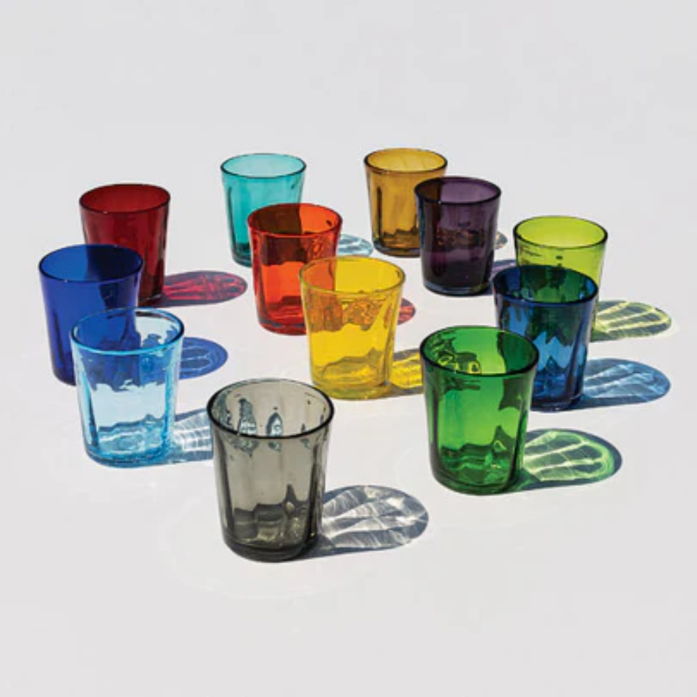 Eleven colored glass glasses in various shades arranged on white background with sharp lights and shadows.